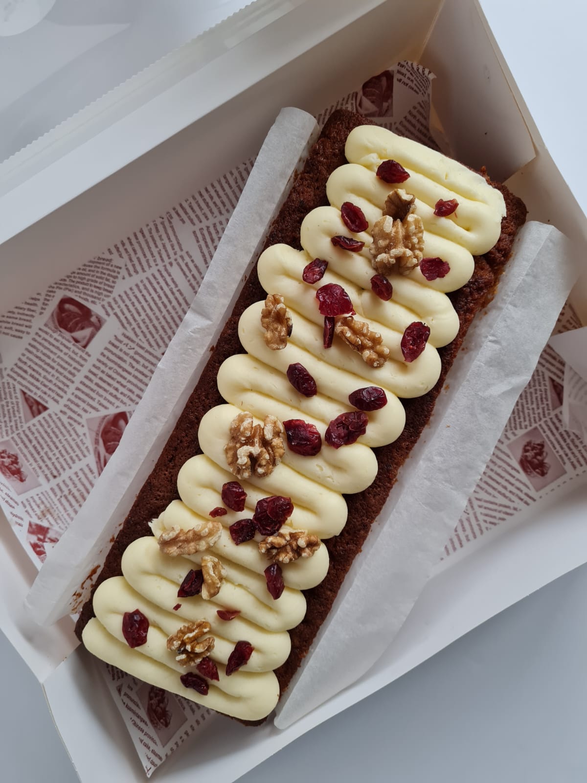 Sugar free banana loaf with piped cream cheese frosting, topped with walnuts and dried cranberries